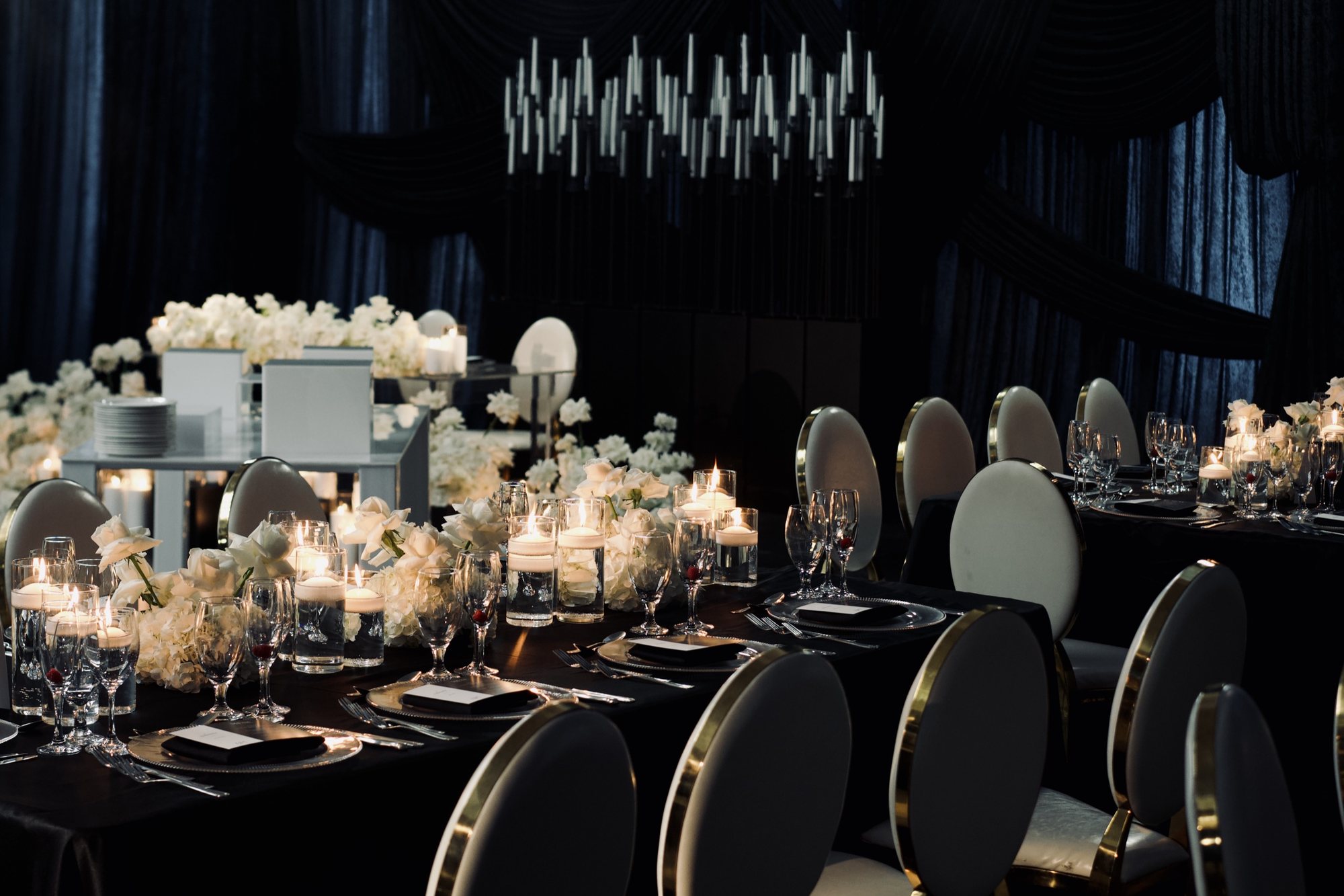 Tables de réception noires décorées de fleurs blanches et de bougies